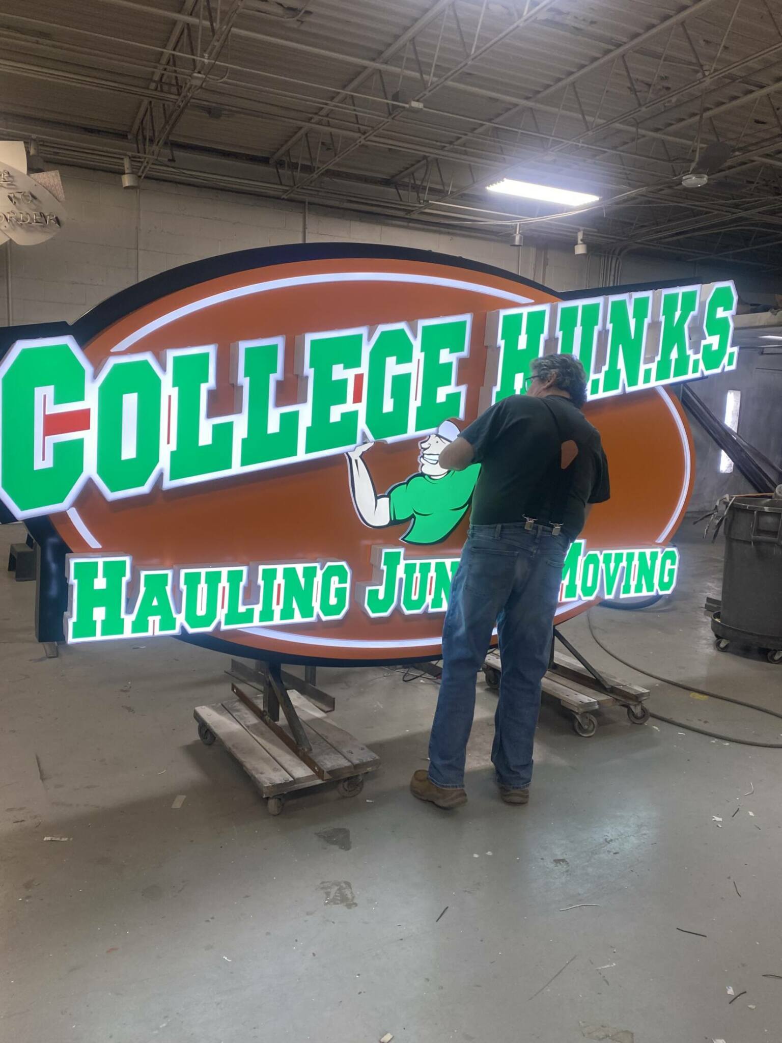 Worker working on wall sign that is completely lit up with the colors white,green and orange.